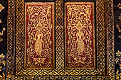 Wat Xieng Thong temple in Luang Prabang, Laos. Detail of a wooden door of the sim with gilded carvings on a red background. 